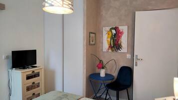 Un dormitorio con cama, televisor en una cómoda, escritorio con silla, cuadro en la pared y una puerta.