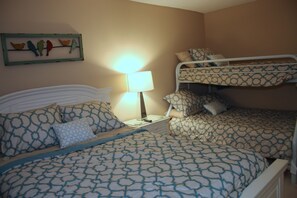 Quarto com beliche, mesa de cabeceira com luminária e decoração de pássaros na parede.
