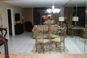 Uma sala de jantar com uma mesa redonda e cadeiras, um lustre e vista para a cozinha através de um painel de vidro.