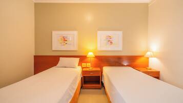 Une chambre d’hôtel avec deux lits simples, des têtes de lit en bois, des tables de chevet avec des lampes et deux œuvres d’art encadrées accrochées au mur.