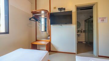 Una camera d'albergo con due letti, una sedia di legno, un televisore montato a parete e un box doccia visibile attraverso una porta aperta.