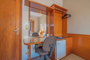 Quarto compacto com guarda-roupa de madeira, escrivaninha, cadeira e um pequeno frigorífico.