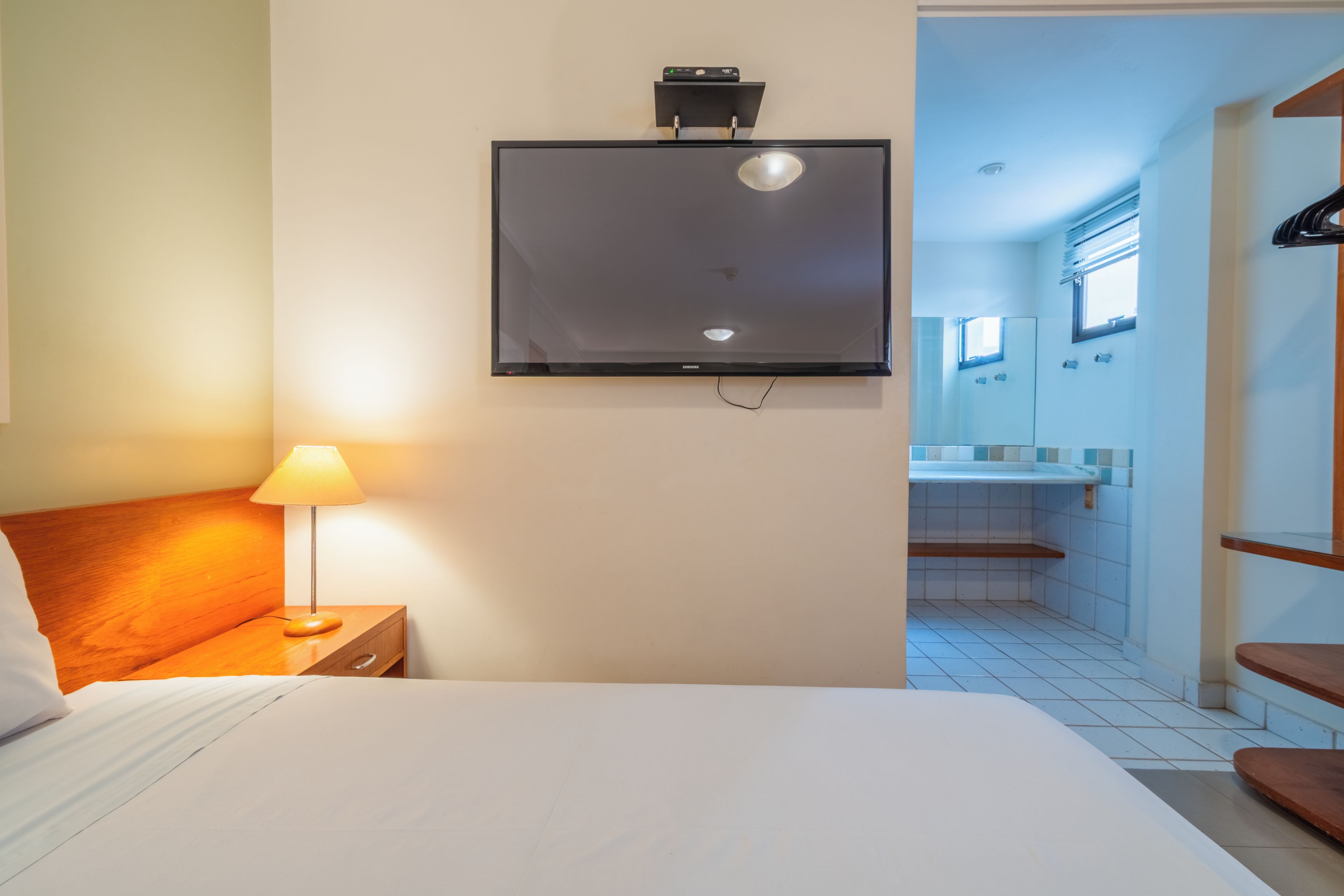A hotel room with a bed, a bedside lamp, a TV mounted on the wall, and a view of the bathroom.