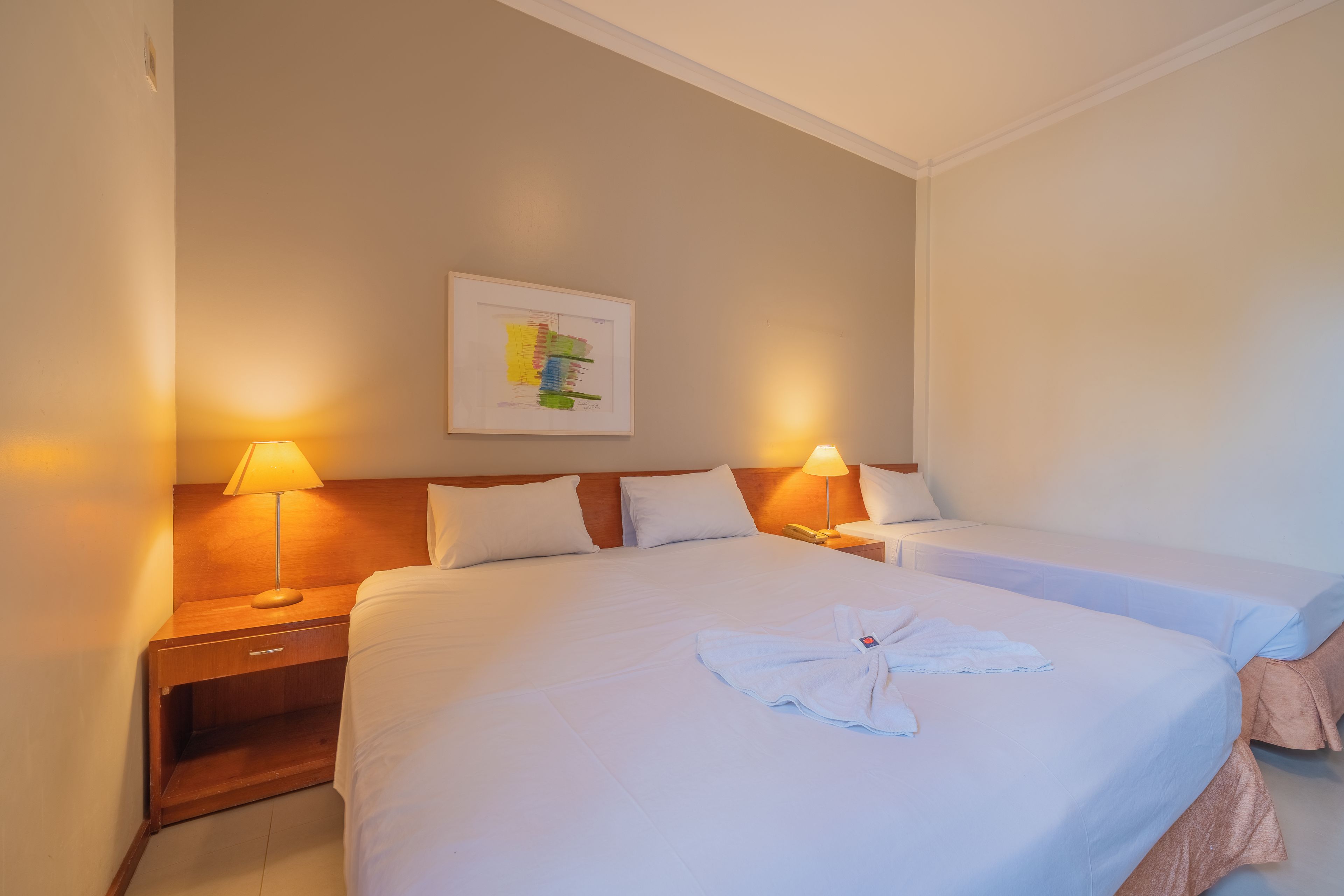 Habitación de hotel con una cama grande, dos mesitas de noche, un cabecero de madera y una obra de arte enmarcada en la pared.