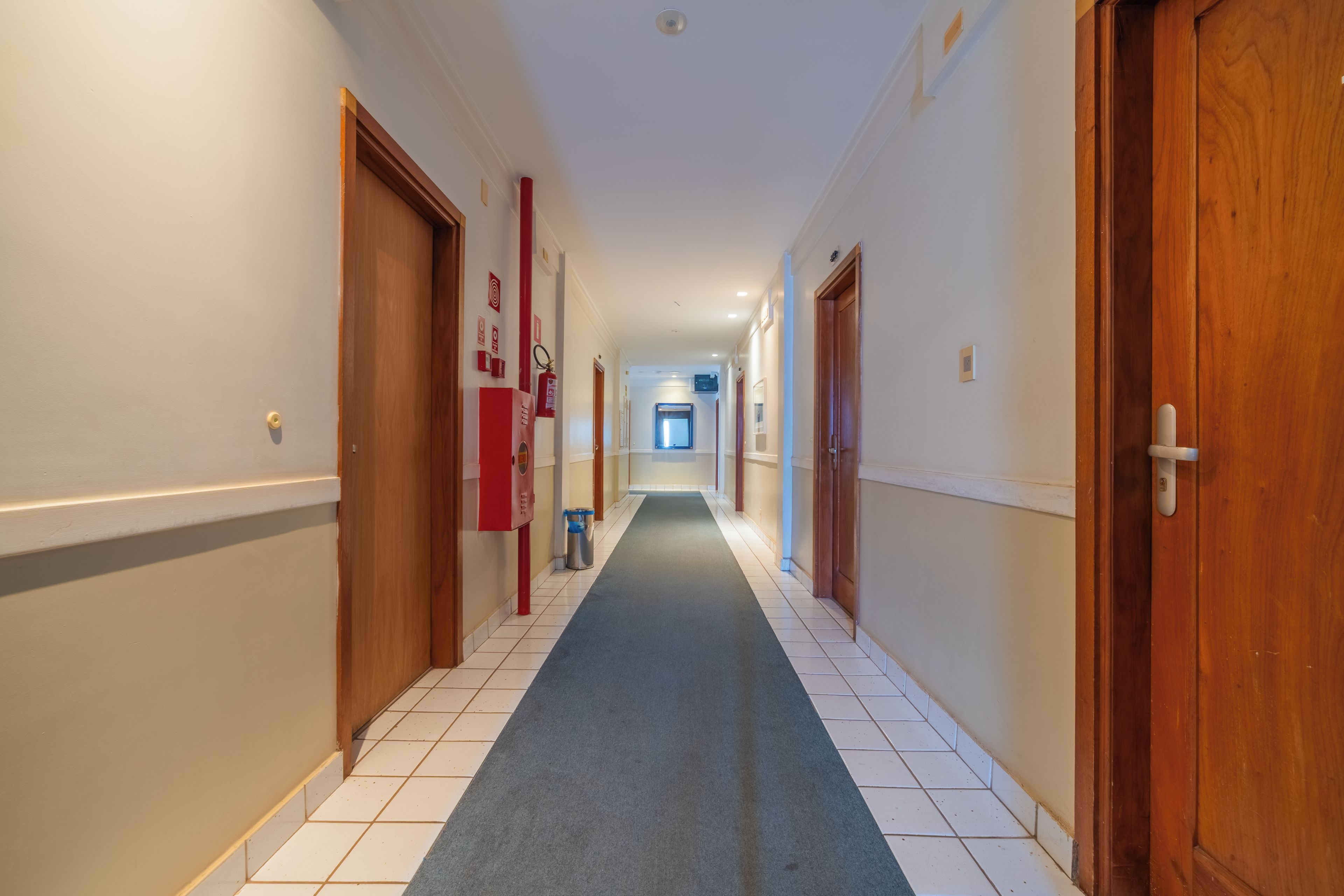 A hotel corridor with wooden doors, a blue carpet, and a fire extinguisher on the wall.