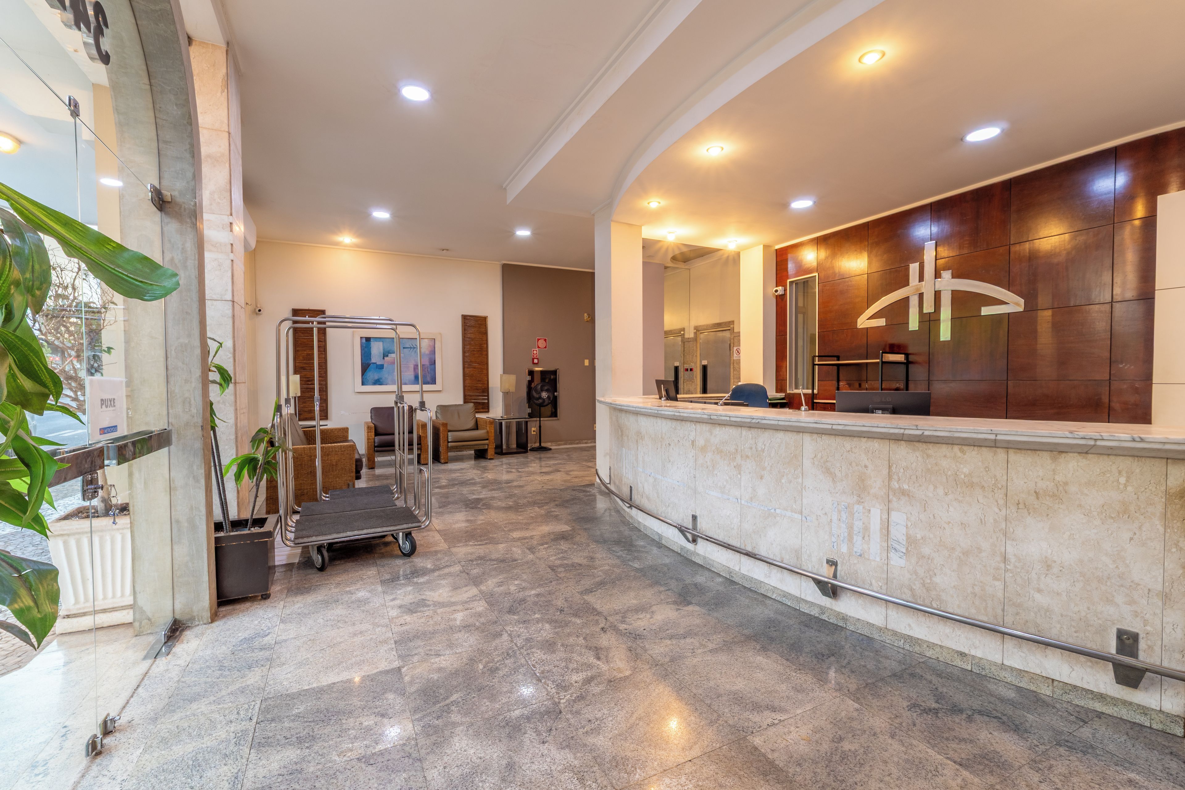 A hotel reception area with a marble counter, a reception desk, and a seating area with chairs.