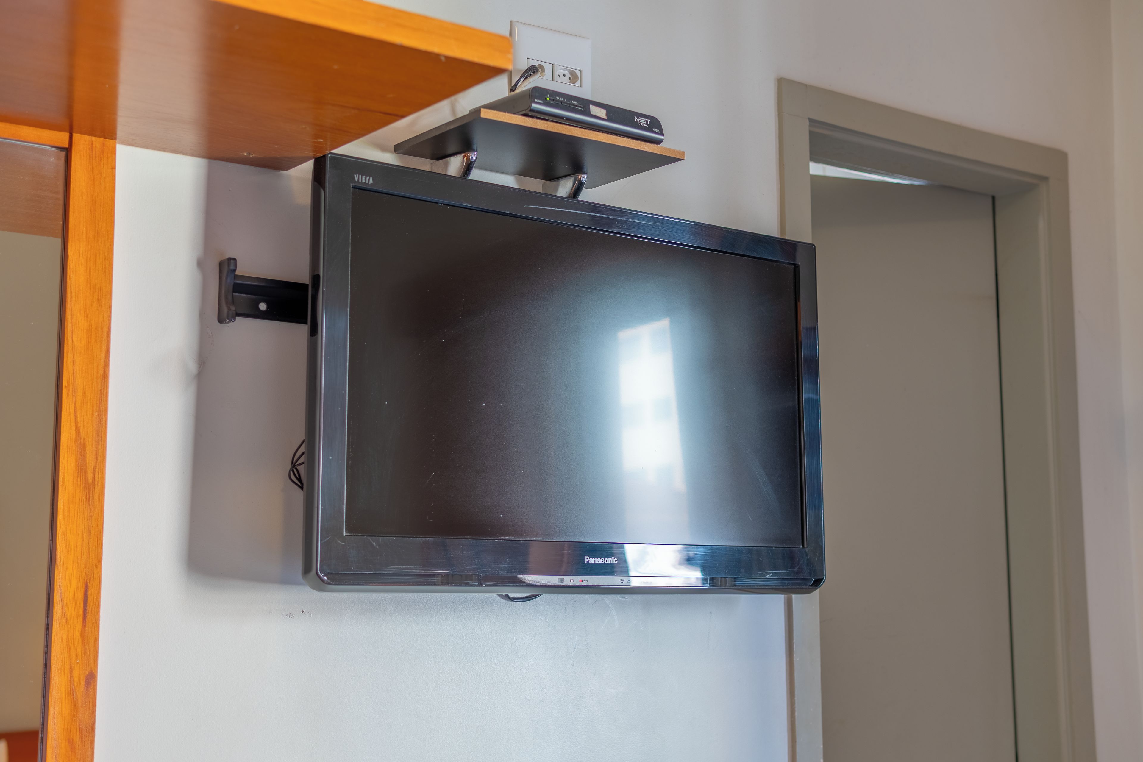 A flat-screen television mounted on a wall with a wooden shelf above it.