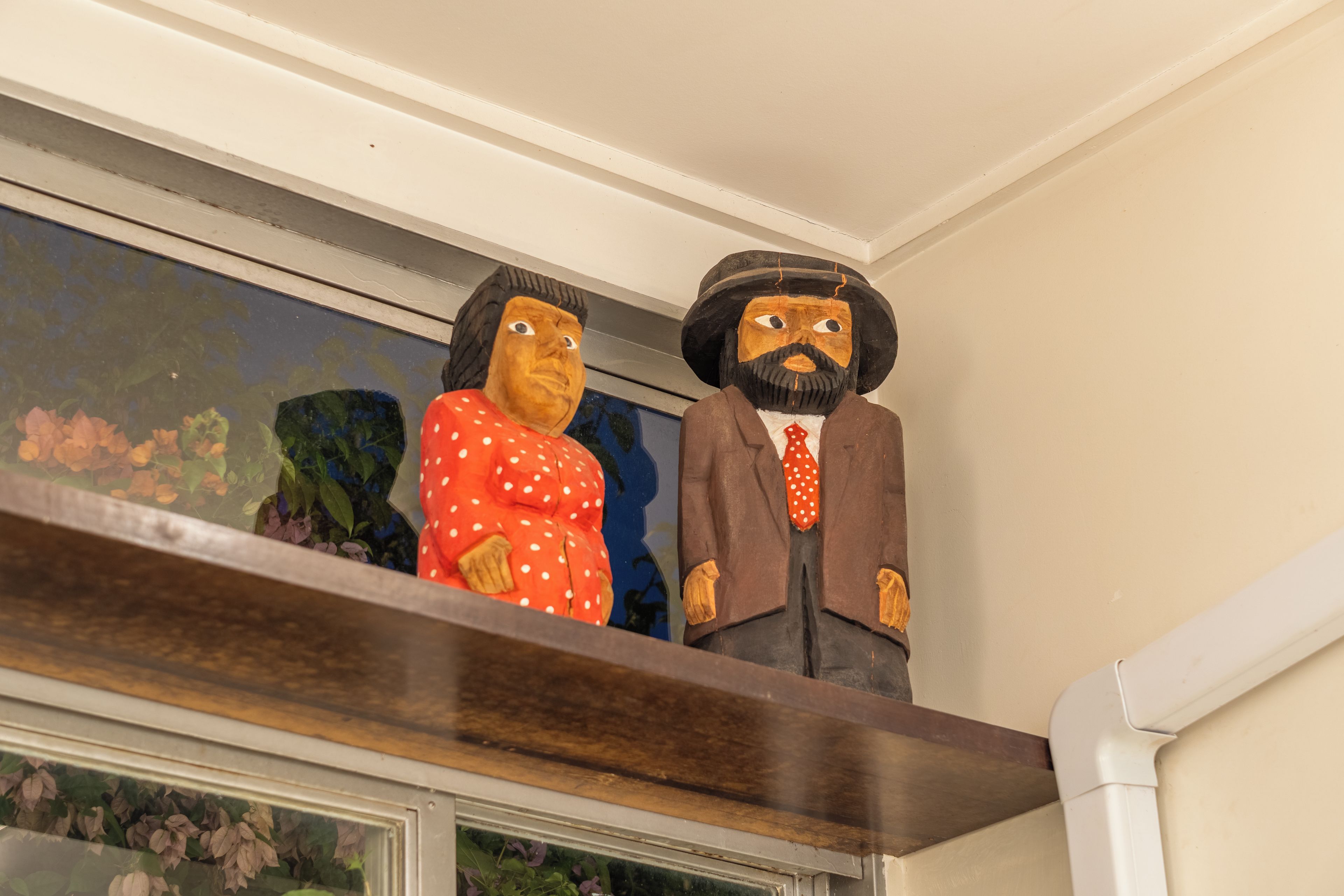 Two wooden sculptures on a shelf above a window.