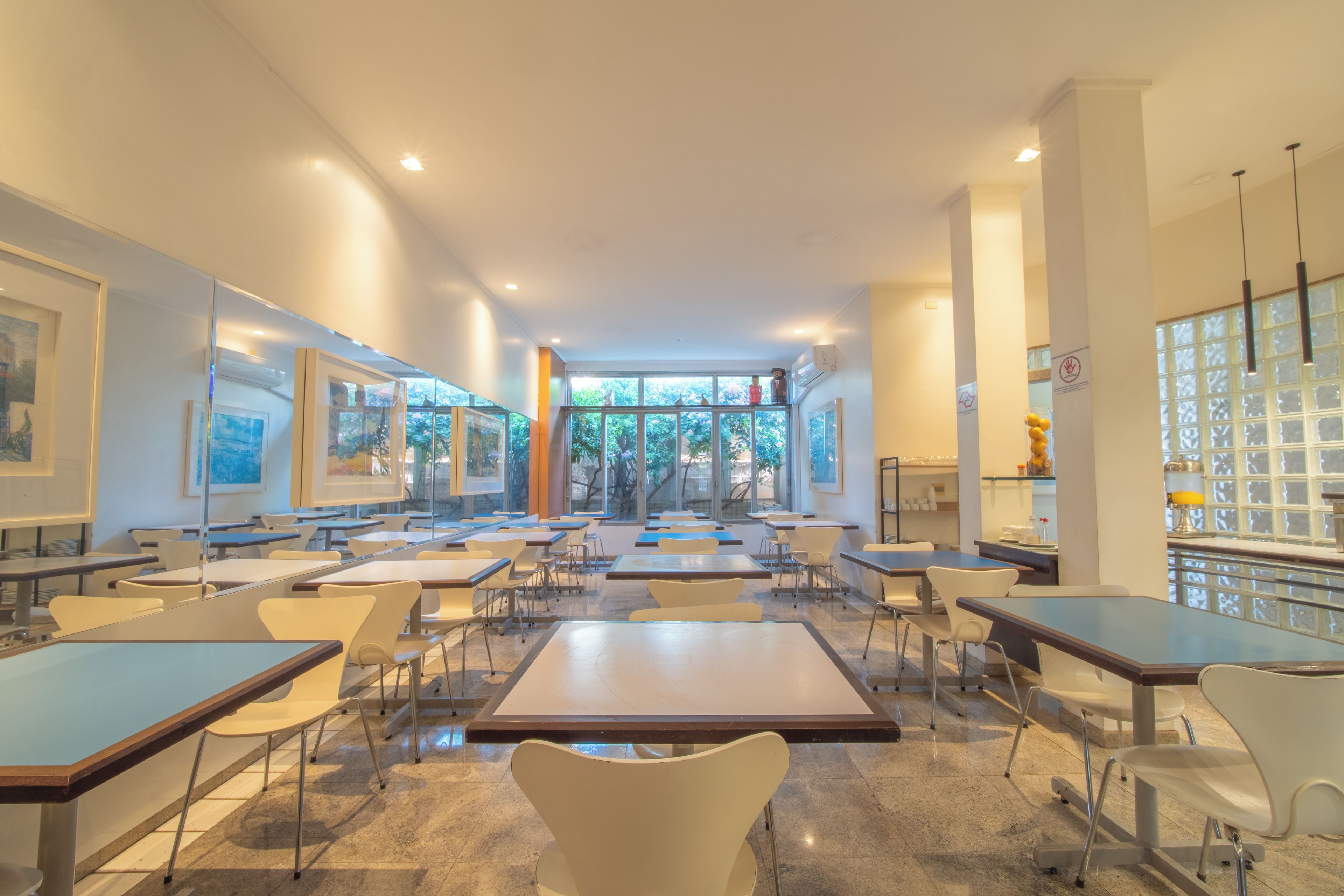 A spacious dining area with tables and chairs, large windows, and artwork on the walls.