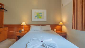 Une chambre d’hôtel avec un lit soigneusement fait, deux lampes de chevet, un téléphone, une table de chevet en bois et une œuvre d’art abstraite encadrée accrochée au mur.