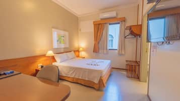 Een hotelkamer met een bed, nachtlampjes, een bureau, een stoel, een raam met gordijnen, een airconditioning en een wandkapstok.