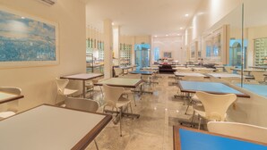 A spacious dining area with multiple tables and chairs, a large painting on the wall, and a view of the kitchen area. - Hotel Metrópolis (São José do Rio Preto)