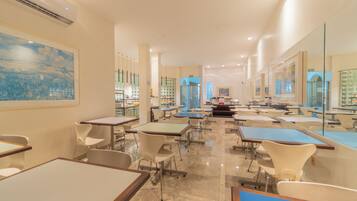 Un vaste espace de salle à manger avec plusieurs tables et chaises, un grand tableau au mur et une vue sur la cuisine.