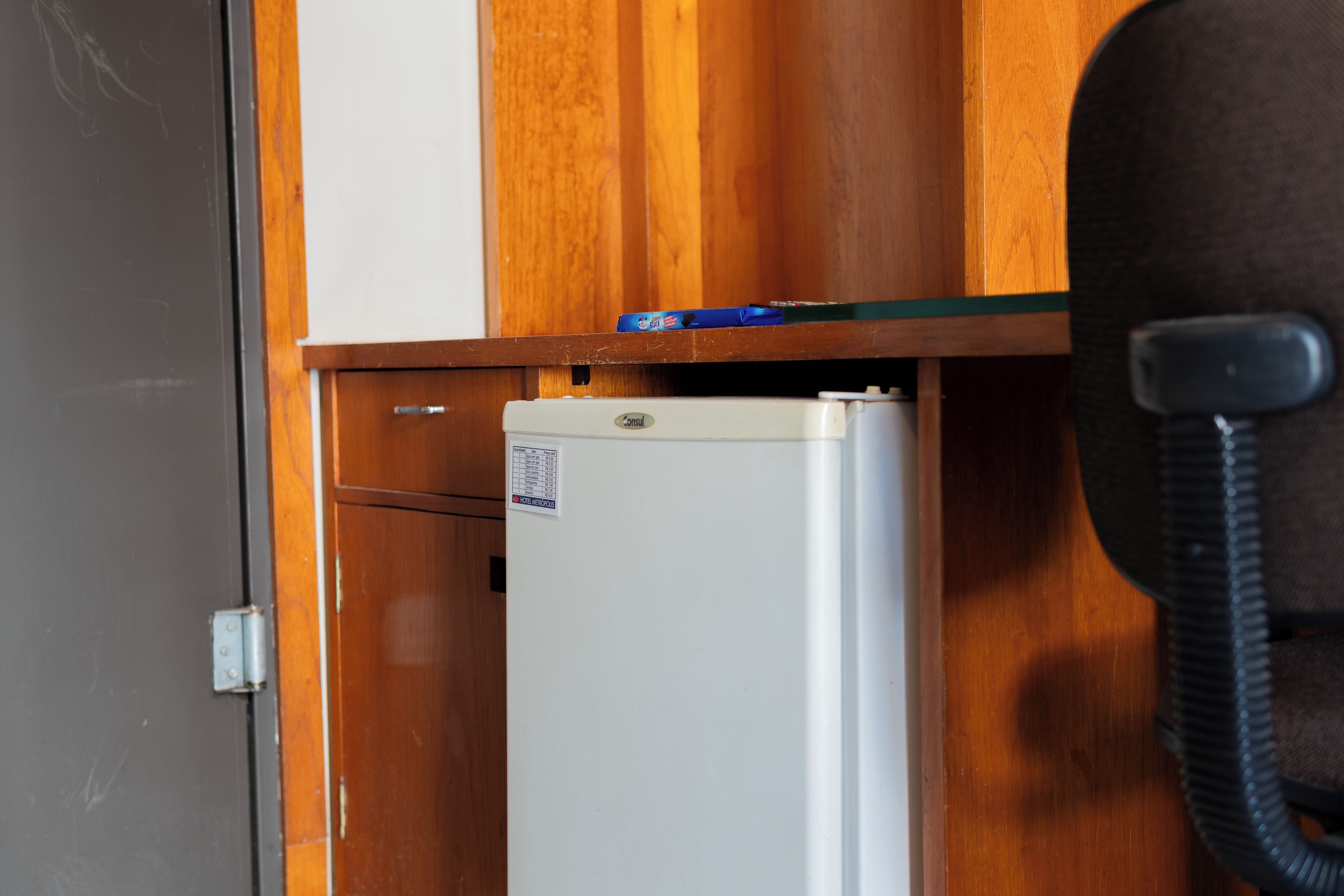 A small white refrigerator with a sticker, a wooden cabinet, and a telephone.