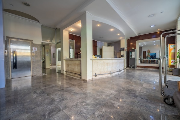 Um hall amplo com piso de mármore, balcão de recepção e geladeira.