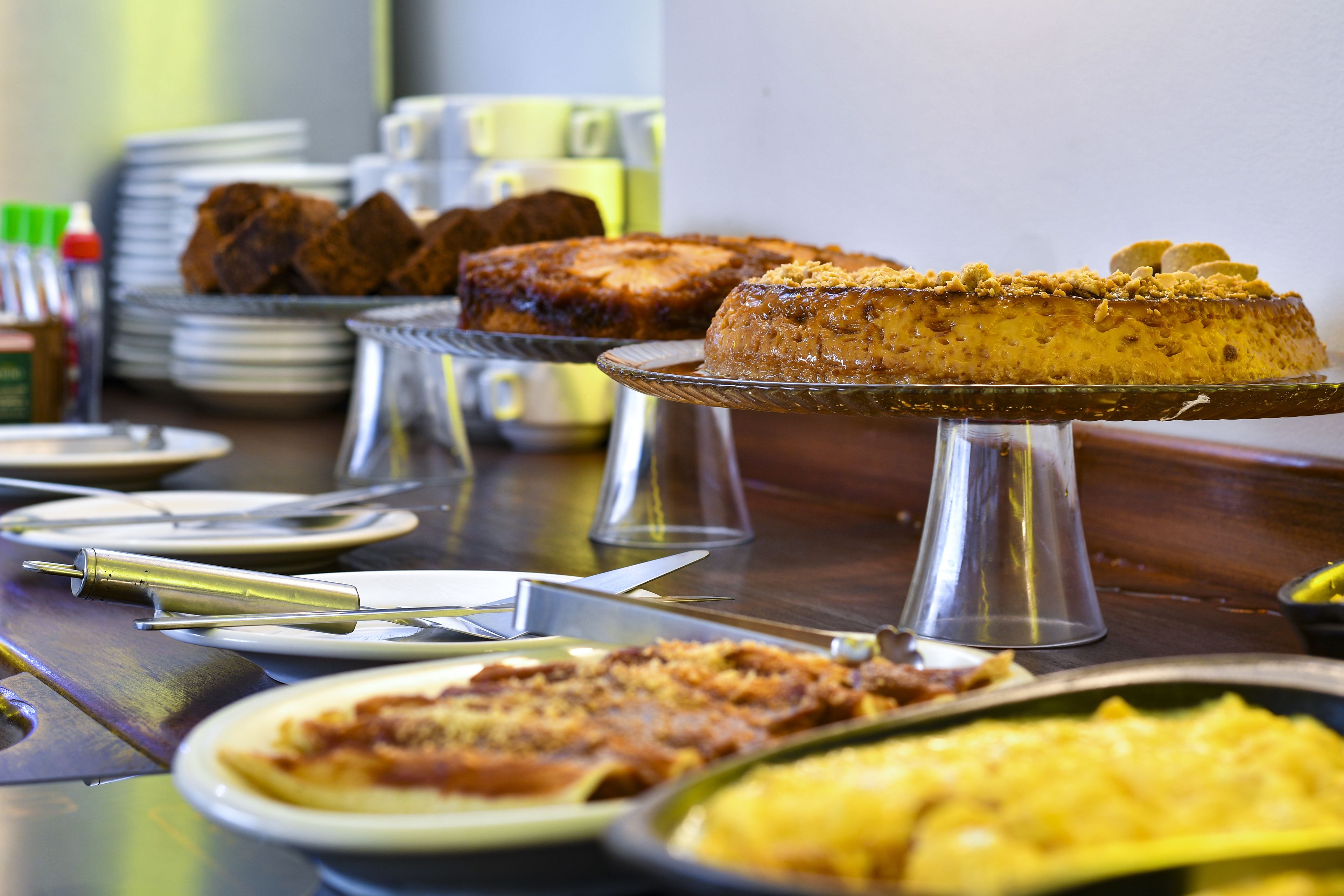 Uma mesa de buffet com diversos pratos, incluindo um bolo em suporte, pratos de comida e talheres.
