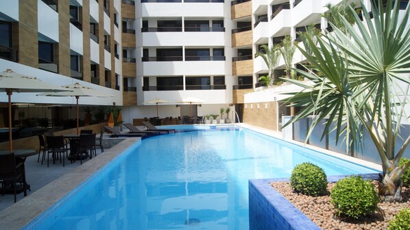 Un hotel moderno con piscina central, asientos exteriores y un edificio de varios pisos con balcones.