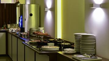 A buffet setup with various dishes and utensils, a refrigerator, and stacked plates.