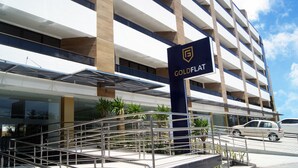 A multi-story hotel with a prominent "GoldFlat" sign, outdoor stairs, and a parking area with cars. - Littoral Gold Flat (João Pessoa)