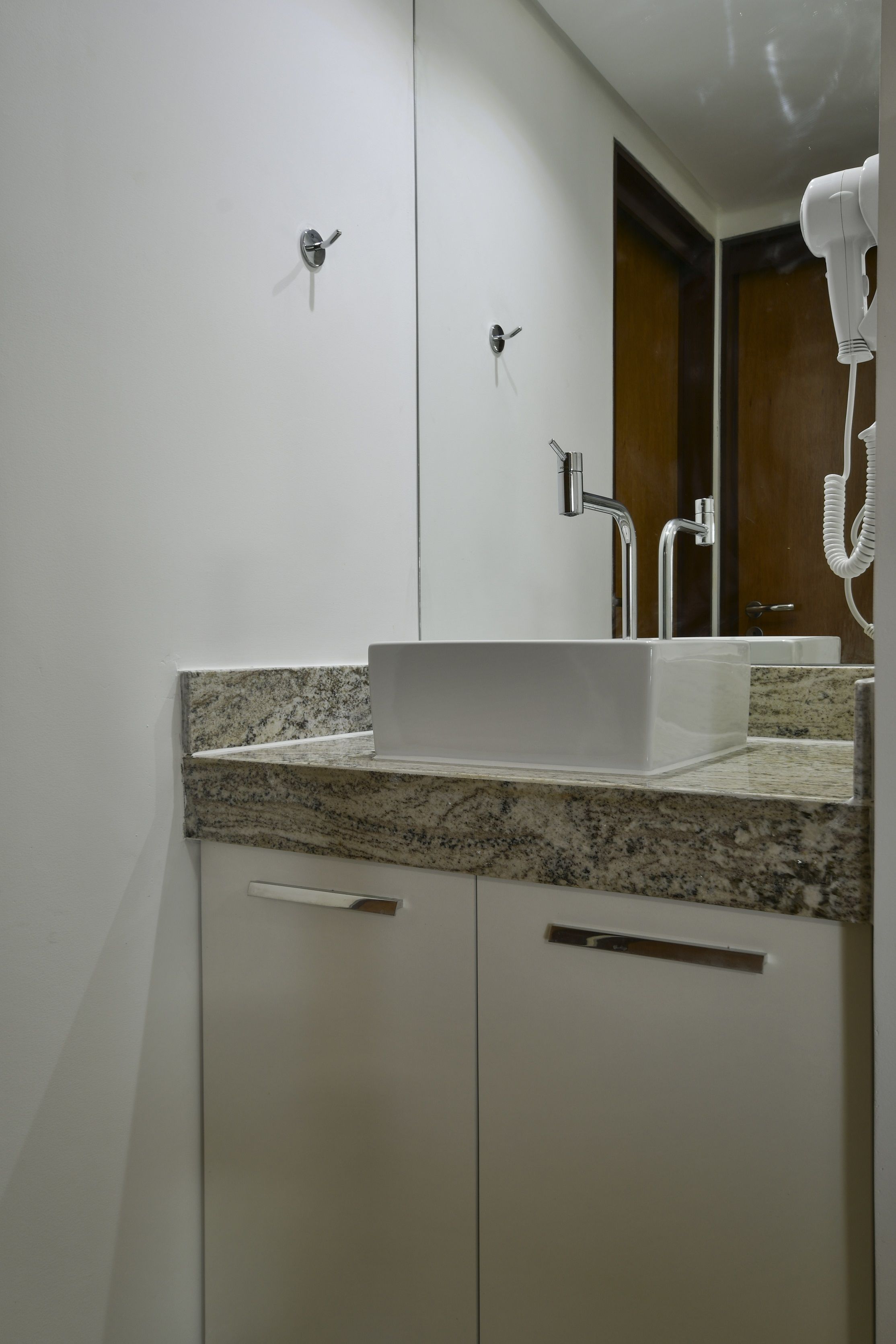 Ein Badezimmer mit einem weißen Waschbecken, einer Granit-Arbeitsplatte und einem an der Wand befestigten Föhn.