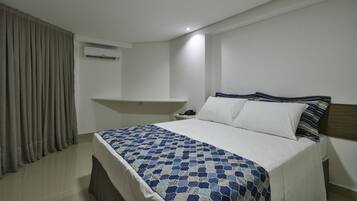 Ein Schlafzimmer mit einem Bett, einem Nachttisch, einer Wand-Klimaanlage und einem Fenster mit Vorhängen.