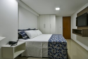 Un dormitorio con cama, mesita de noche con teléfono, armario y televisión montada en la pared.