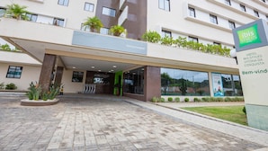 Entrada de un hotel con un camino adoquinado, un letrero de 'ibis Styles Hotels' y una placa con el nombre 'Vitória da Conquista'.