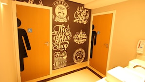 Un baño con una pared decorada con frases y símbolos relacionados con el café, un secador de manos y un dispensador de papel higiénico.