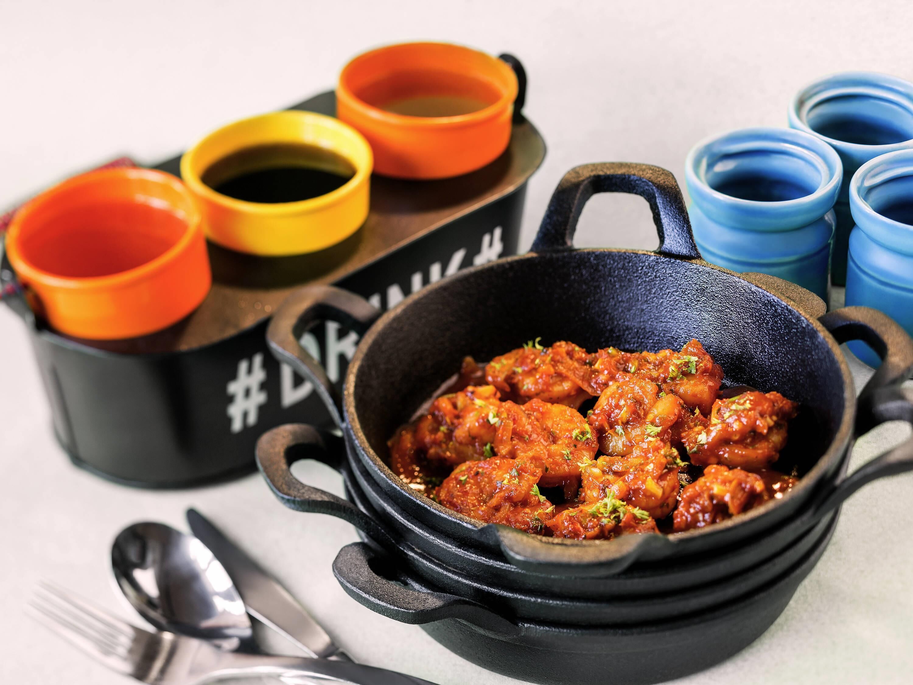 A black cast iron skillet filled with a red dish, accompanied by three small bowls with different colored contents and a spoon.