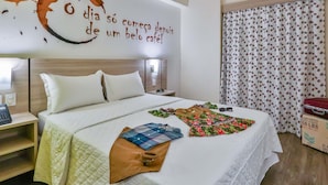 Una habitación de hotel con cama, mesita de noche, un cuadro con motivos de café, cortina y maleta.