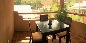 A balcony with a table and chairs, a potted plant, and a view of neighboring houses.
