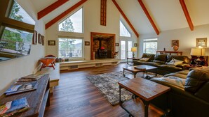 A spacious living room with a high ceiling, wooden beams, a fireplace, and large windows offering a view of the outdoors. - 7 Mi to Bass Lake! Spacious 'Mudge Ranch Retreat' (Coarsegold)