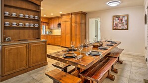 A spacious kitchen with wooden cabinets, a large dining table set for six, and a built-in shelf with decorative mugs. - 7 Mi to Bass Lake! Spacious 'Mudge Ranch Retreat' (Coarsegold)