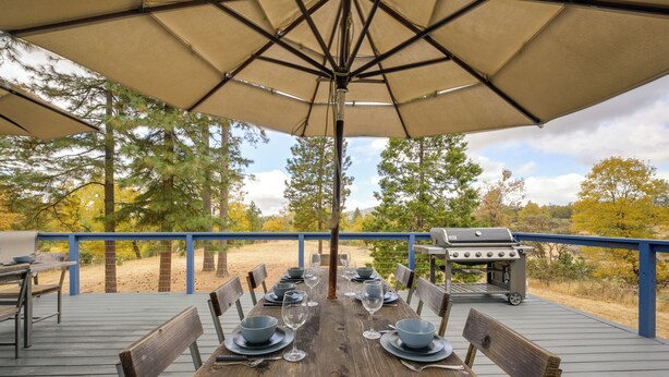 A wooden deck with a table set for dining, an umbrella, and a grill. - 7 Mi to Bass Lake! Spacious 'Mudge Ranch Retreat' (Coarsegold)