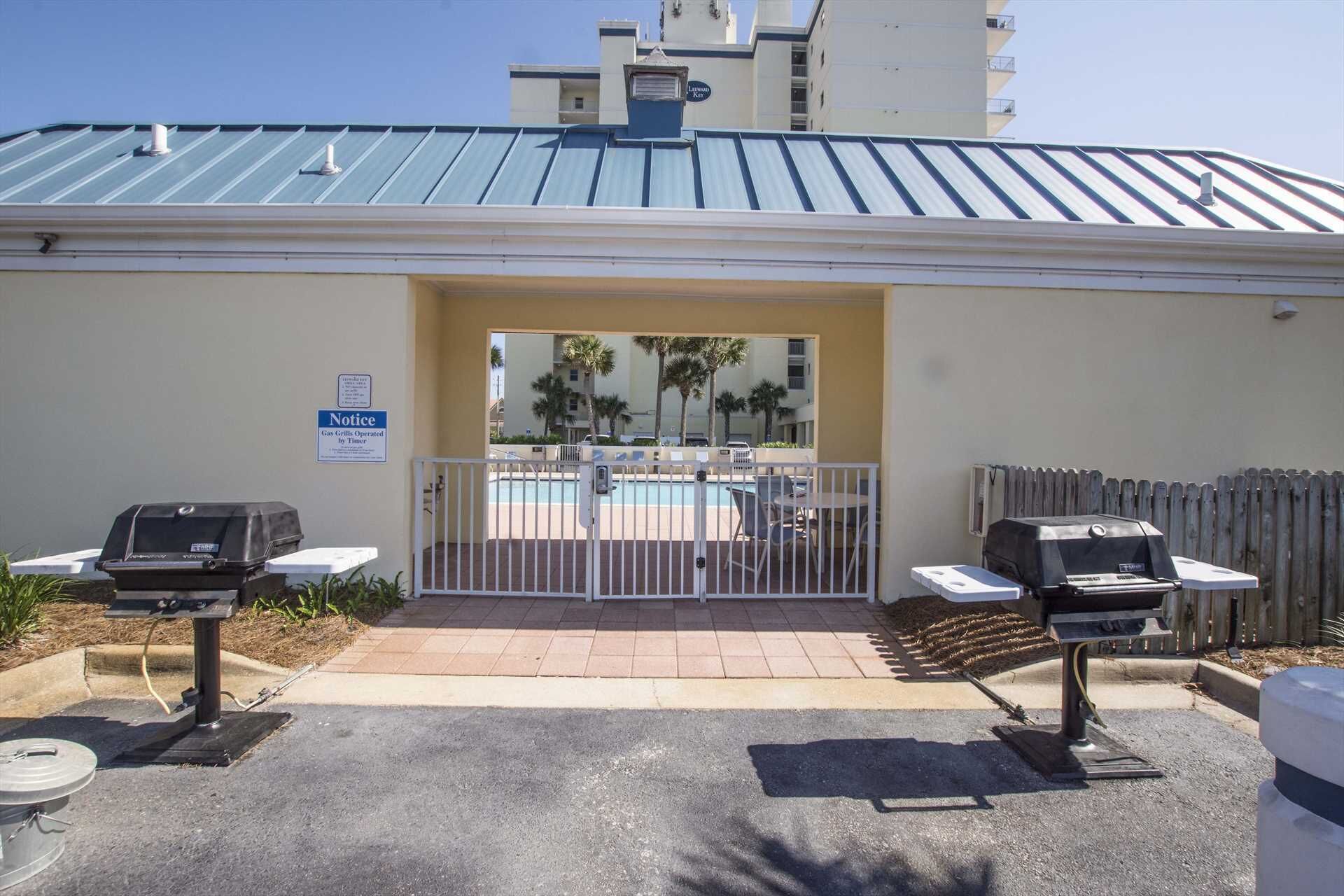 A poolside area with a covered patio, two barbecue grills, and a sign indicating gas grills operated by timer.