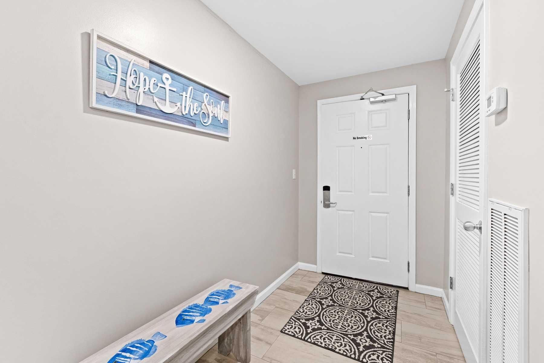 A hallway with a white door, a bench with blue fish designs, and a patterned rug.