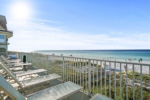 Un balcon avec des chaises longues donnant sur une plage, sous un ciel dégagé.