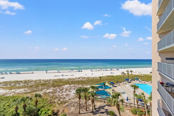 A beach view from a hotel balcony with a pool and lounge chairs.