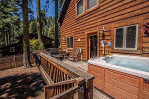 A wooden cabin with a hot tub, deck chairs, and a wooden fence.