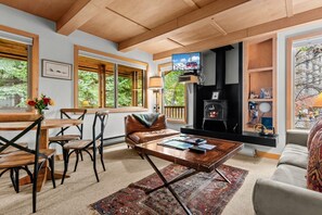 A cozy living room with a fireplace, wooden furniture, and large windows. - RMR: La Choumine 6 Condo in Teton Village / Steps from the Mountain! (Teton Village)
