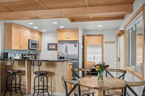 A modern kitchen with wooden cabinets, a stainless steel refrigerator, and a bar area with stools. - RMR: La Choumine 6 Condo in Teton Village / Steps from the Mountain! (Teton Village)