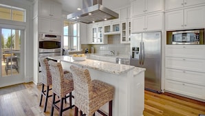 A modern kitchen with white cabinetry, stainless steel appliances, and a central island with bar stools. - Beautiful Beach Home in Cinnamon Shore w/Gulf Peeks & Access to Amenities (Port Aransas)