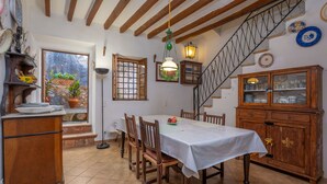 A dining area with a table set for four, wooden chairs, a cabinet with glass doors, a staircase, and a window with a view of plants outside. - CA NA CARME (CA NA CARME ALARONERA) - Chalet for 4 people in Alaro. Free WiFi (Alaró)