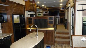 A compact kitchen with wooden cabinets, a stainless steel sink, a microwave, and a built-in oven. - Luxury RV at Bolton Bay on Long Lake (Park Rapids)