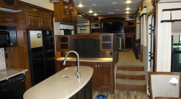 A compact kitchen with wooden cabinets, a stainless steel sink, a microwave, and a built-in oven.