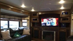 A living room with a fireplace, a leather couch, and a television. - Luxury RV at Bolton Bay on Long Lake (Park Rapids)
