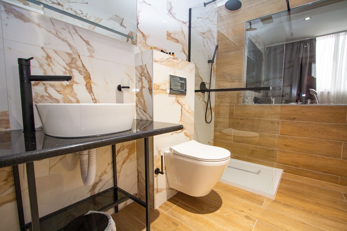 Ein modernes Badezimmer mit Waschtisch aus Marmor, Toilette und einer Duschkabine.