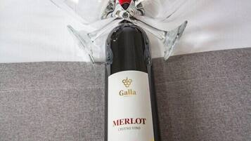 Een fles Galla Merlot wijn met een helder glazen strik erop, geplaatst op een grijze stoffen ondergrond.