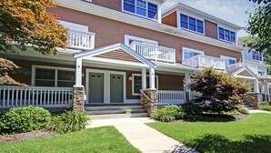 A multi-story residential building with a front porch, stone pillars, and a well-maintained lawn. - Water Street Townhouses (Saugatuck)