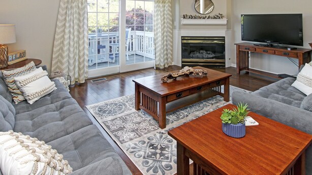 A living room with a sofa, a coffee table, a fireplace, a television, and a view of the outdoors. - Water Street Townhouses (Saugatuck)